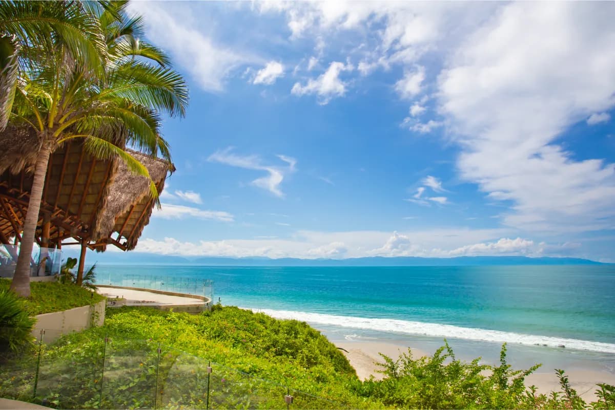 Turquoise waters and pristine sandy beach viewed from the resort cliffside with thatched palapa and tropical vegetation