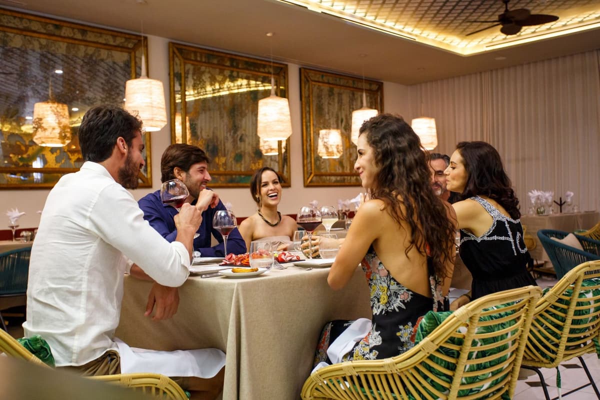 Beachfront restaurant terrace with ocean views, elegant table settings, and thatched palapa roof at sunset