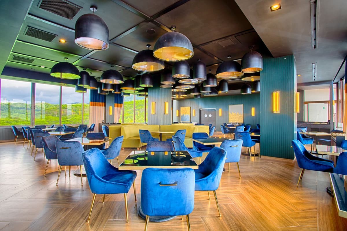 Stylish restaurant interior with contemporary blue velvet seating, pendant lighting, and floor-to-ceiling windows