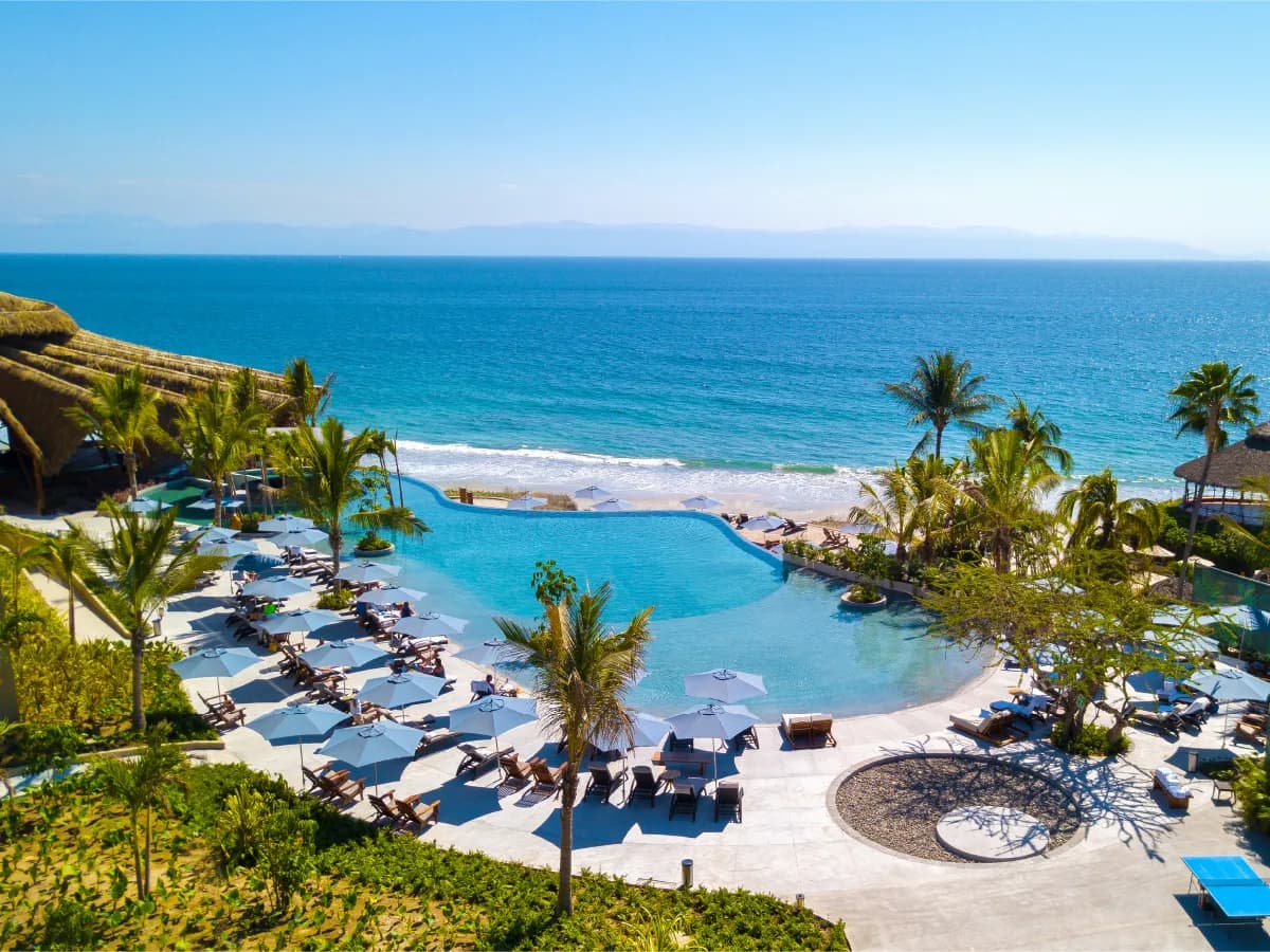 The main beachfront infinity pool with sun loungers, palm trees, and panoramic views of Banderas Bay