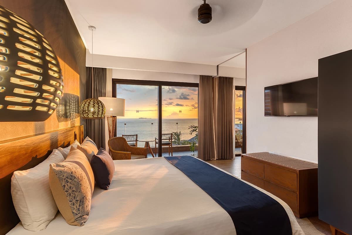 Ocean view king bedroom with artisan lighting, warm wood accents, and a balcony overlooking the Pacific sunset