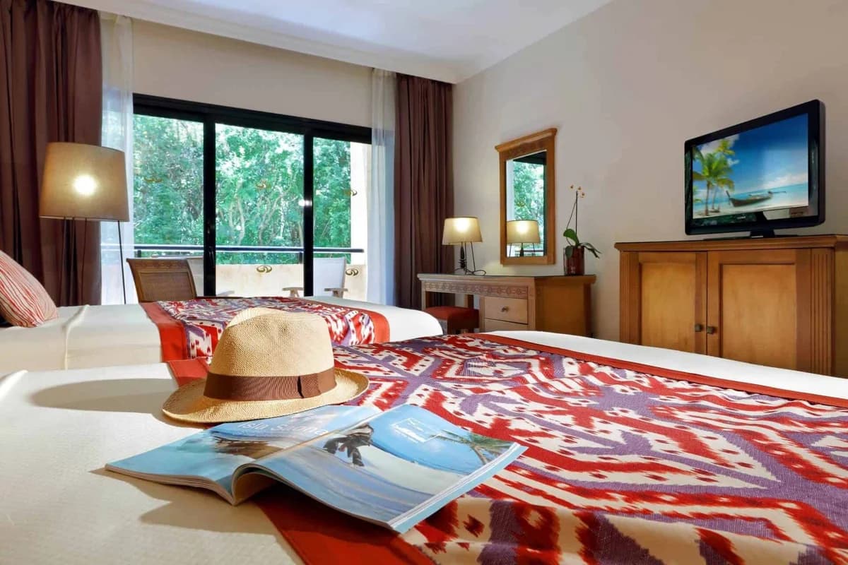 Deluxe Garden View room with king bed, flat-screen TV, minibar, and furnished balcony overlooking tropical gardens