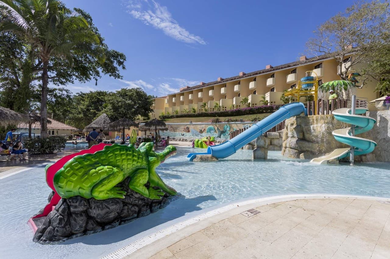 Children's water park with mini slides, palm tree sprinklers, and shallow splash pools