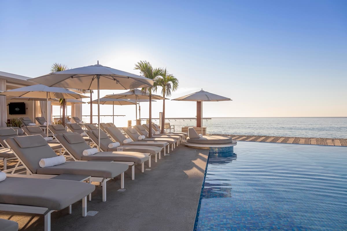 Beachfront infinity pool with plush loungers and ocean views at sunset