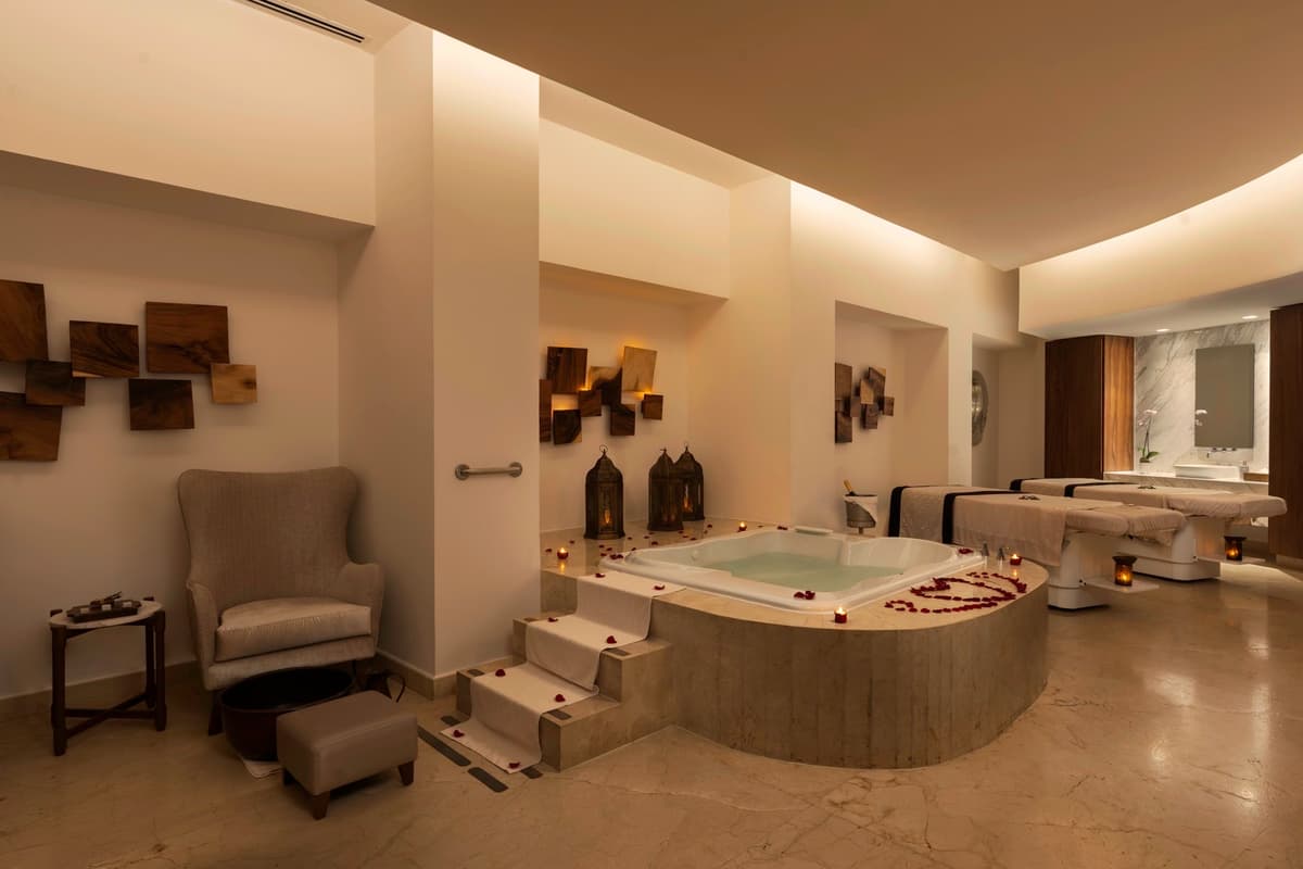 Couples spa suite with hydrotherapy tub, massage beds, and rose petals