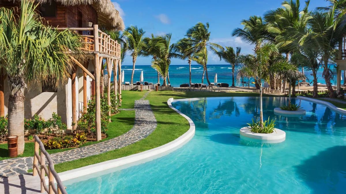 Beachside pool area with stone pathway, garden plantings, and ocean views through the palms