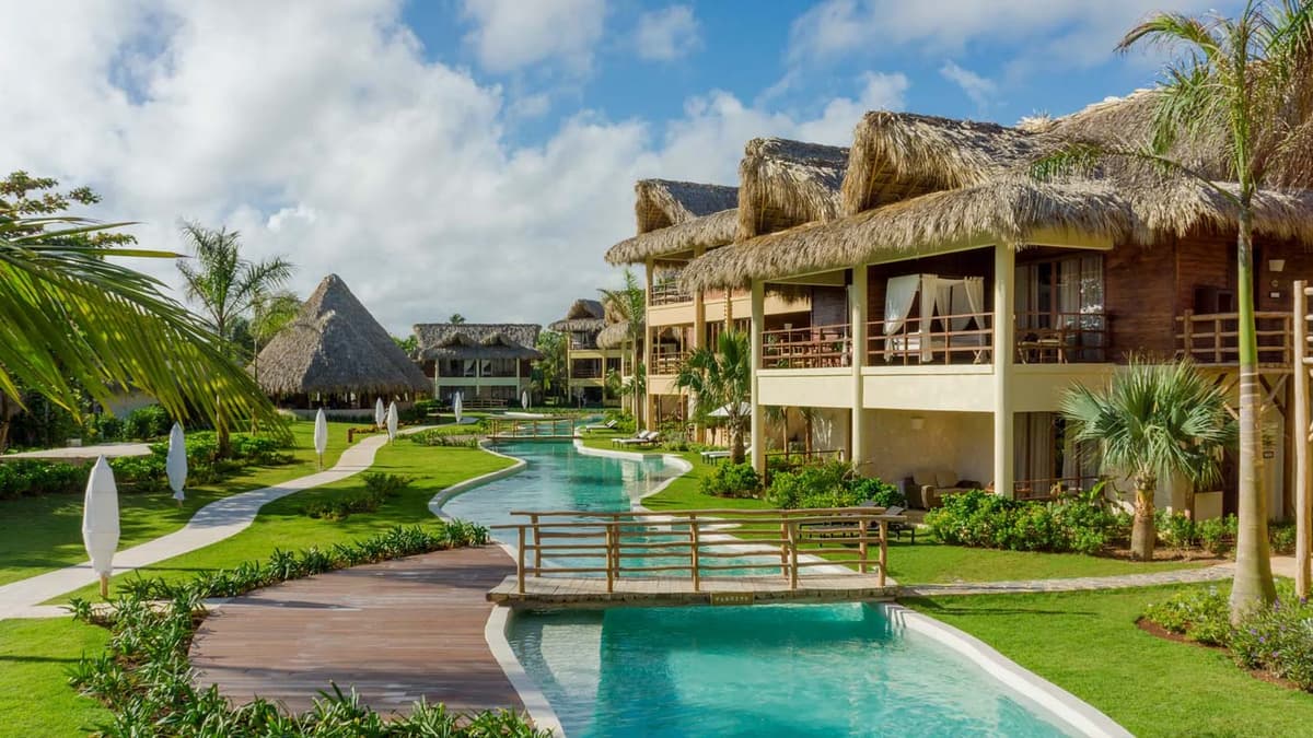Serpentine infinity pool winding through tropical gardens with wooden bridges connecting suite buildings