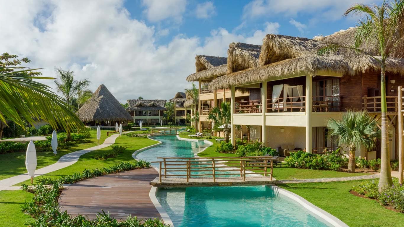 Serpentine infinity pool winding through tropical gardens with wooden bridges connecting suite buildings
