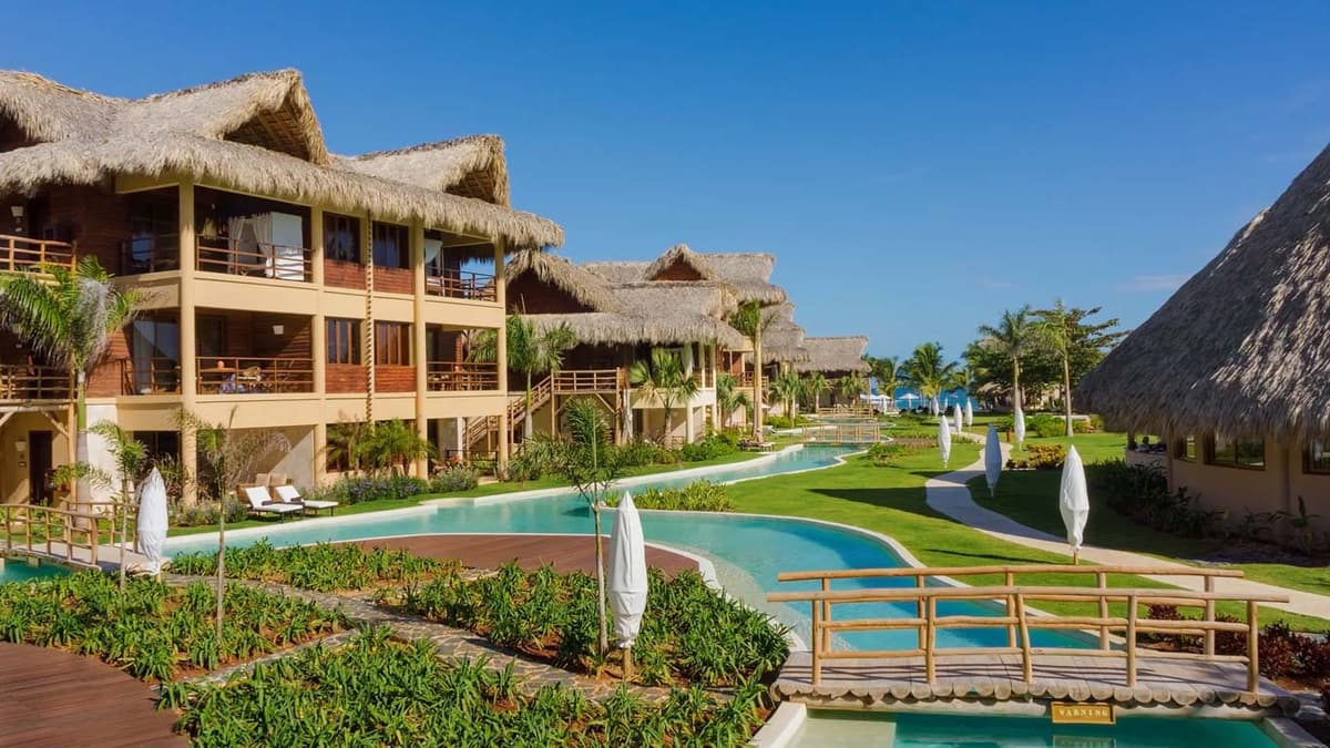 Winding pool channels connecting palapa-roofed buildings with the Caribbean Sea visible in the background