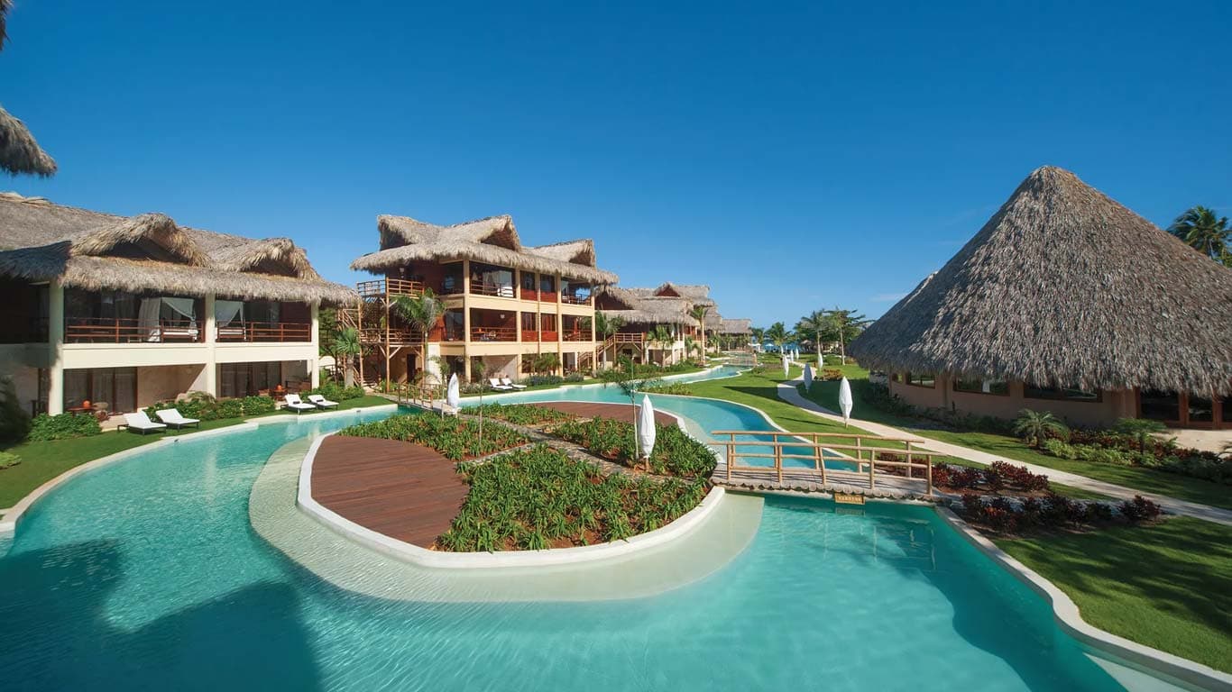 Expansive view of the main serpentine pool with Balinese daybeds, wooden deck islands, and tropical garden plantings