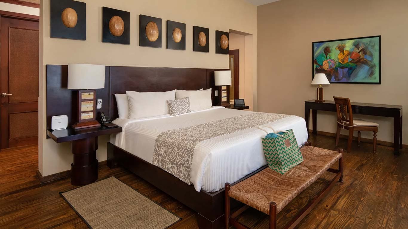 Junior Suite bedroom with king bed, Dominican artwork, hardwood floors, and teak furniture