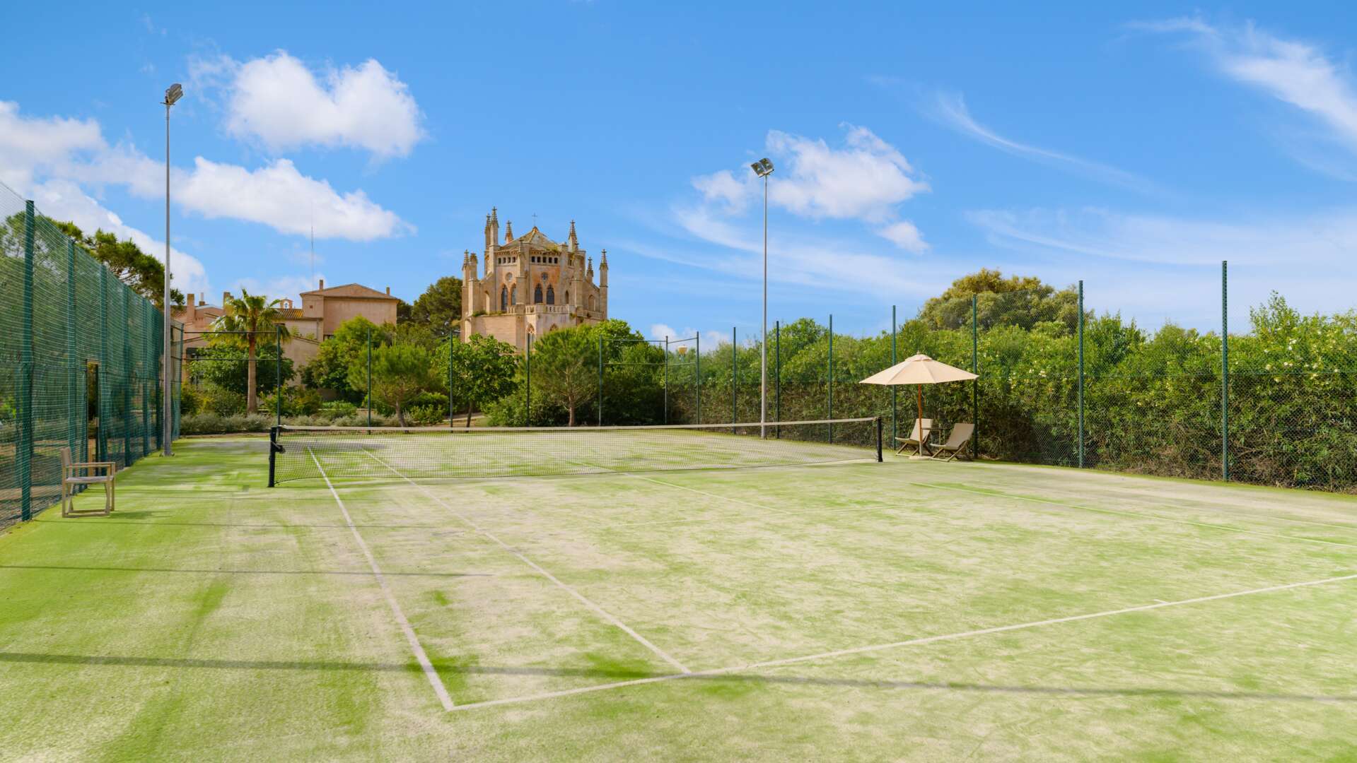 Tennis court set against the dramatic backdrop of the neo-Gothic La Gran Cristiana chapel and Mediterranean greenery
