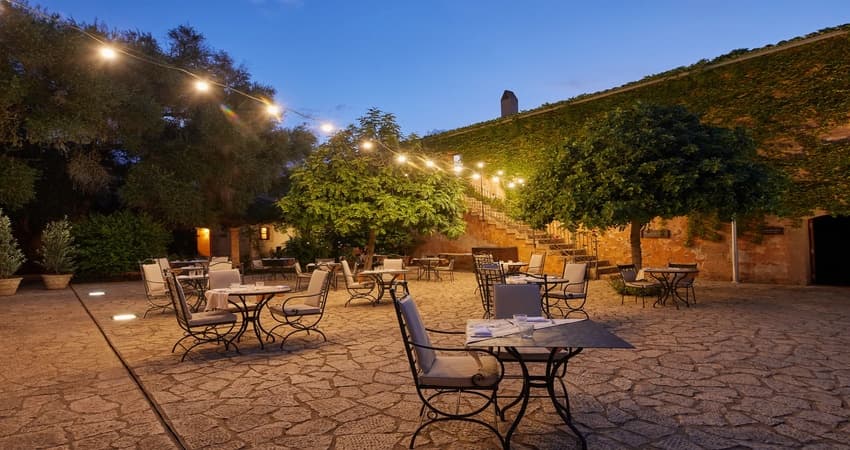 Ses Bovedes Gastro Bar courtyard at twilight with festoon lighting, ivy-clad walls, and a view of the historic windmill tower