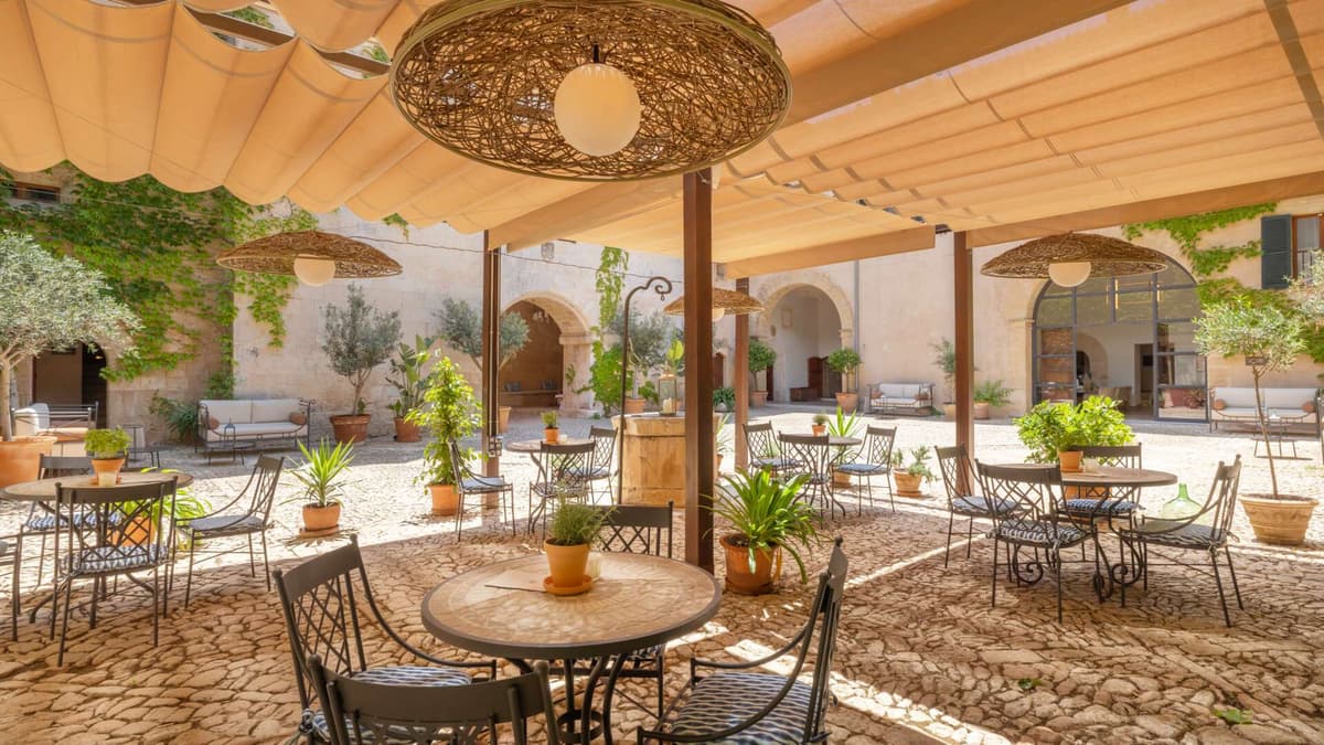 Historic courtyard dining area with canvas awnings, woven rattan pendants, potted olive trees, and stone archways of the original manor
