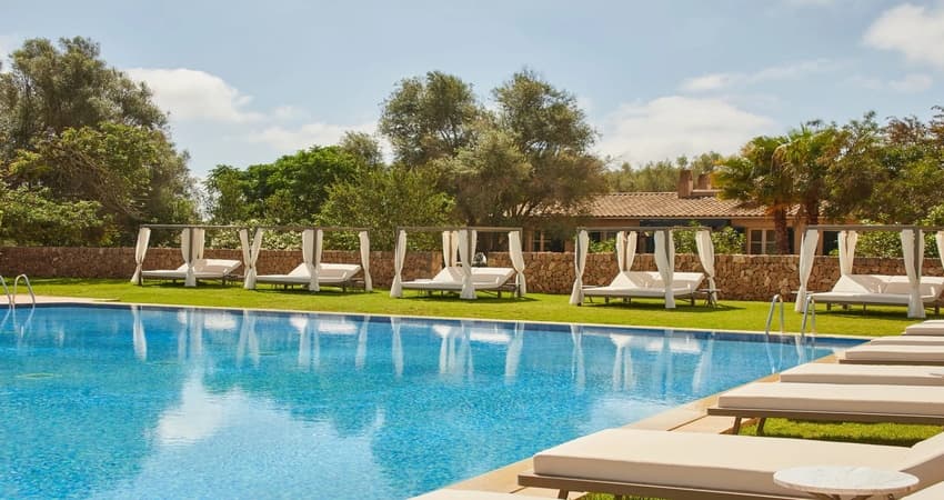 Main outdoor pool with white Bali daybeds on manicured lawns, backed by olive trees and traditional stone walls