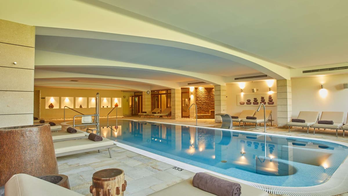 Expansive indoor spa pool with curved contemporary ceilings, stone accents, and integrated hydrotherapy stations