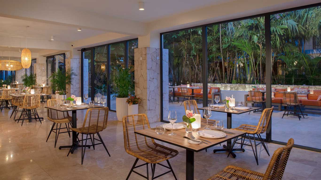 Bloom Restaurant interior with rattan chairs, stone columns, and tropical garden views at night