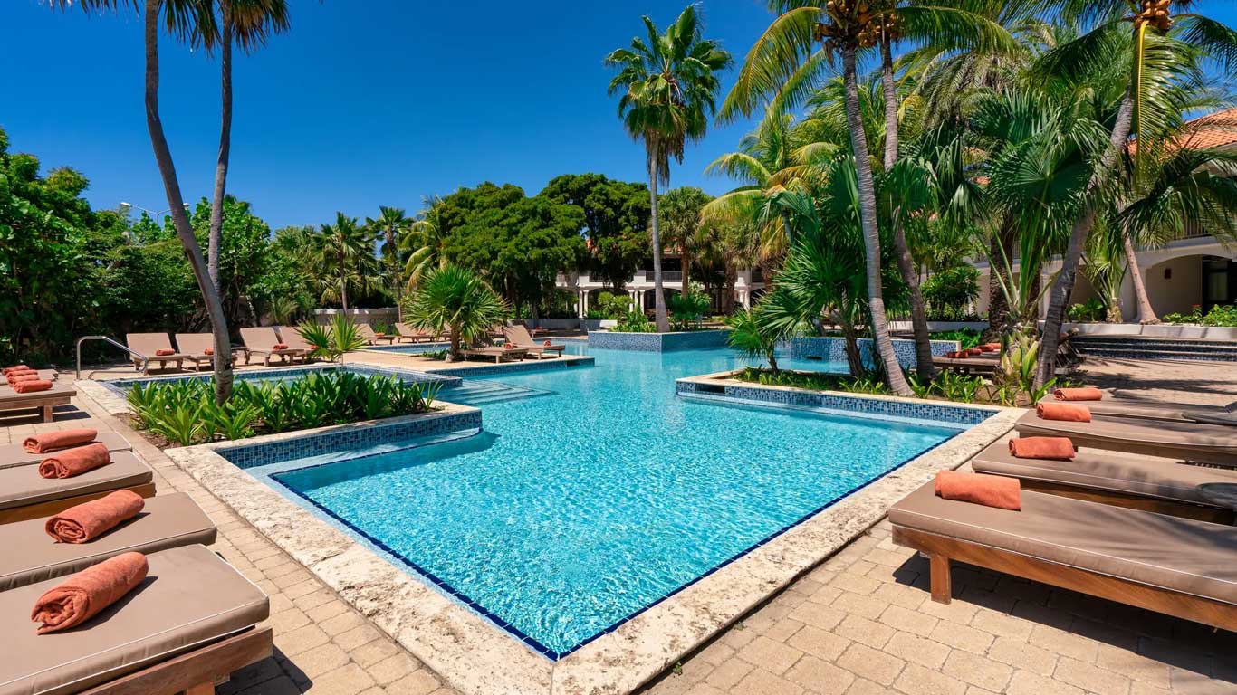 Resort pool with coral-orange towel service and palm-shaded loungers