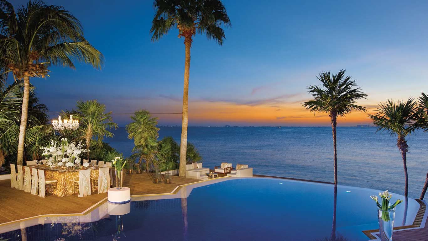 Infinity pool and oceanfront terrace at sunset with palm trees and Caribbean Sea views