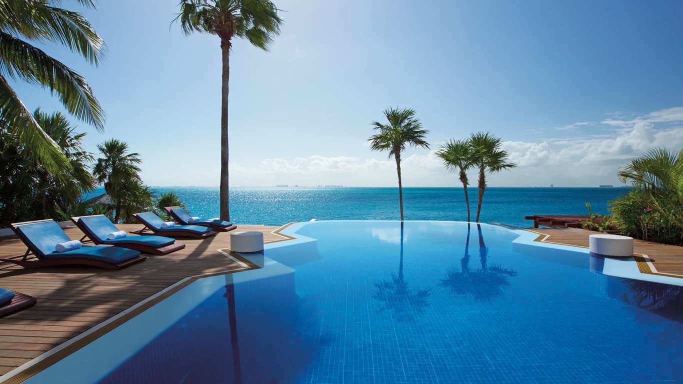 Main infinity pool with palm trees and unobstructed Caribbean Sea views toward Cancun