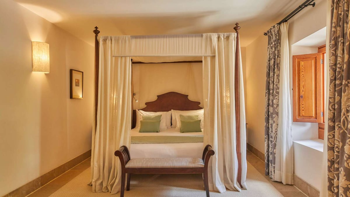 Double Tramuntana Room with classic four-poster canopy bed, sage green accents, and warm amber lighting