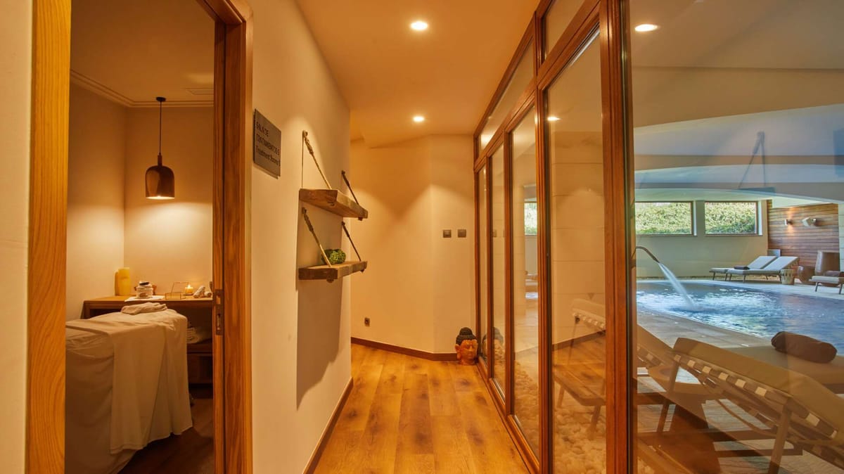 Spa treatment room entrance with warm wood finishes and glass wall overlooking the indoor hydrotherapy pool